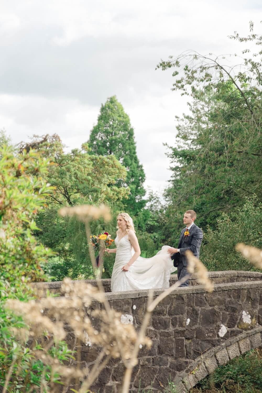 Groom walking behind the bride as she holds her dress at Foxtail Barns
