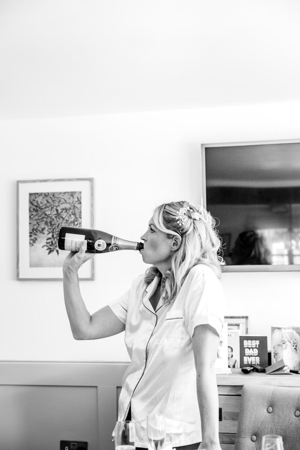 Bride laughing with a swig of champagne during bridal preparations