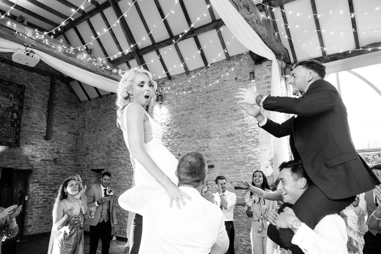 Bride and groom on the shoulders of guests at The Great Barn, Aynho