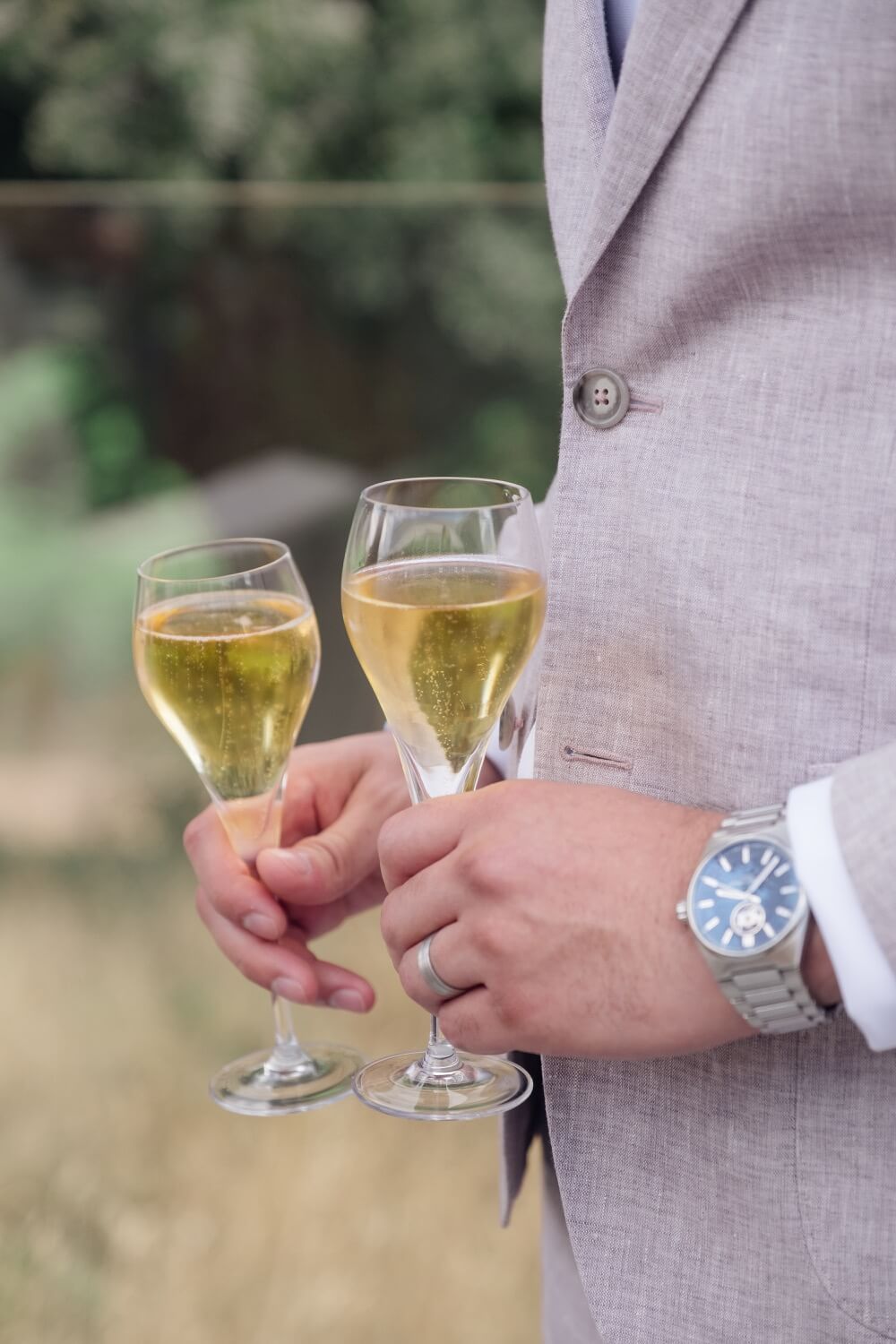 The groom holding two glasses of sparkling wine