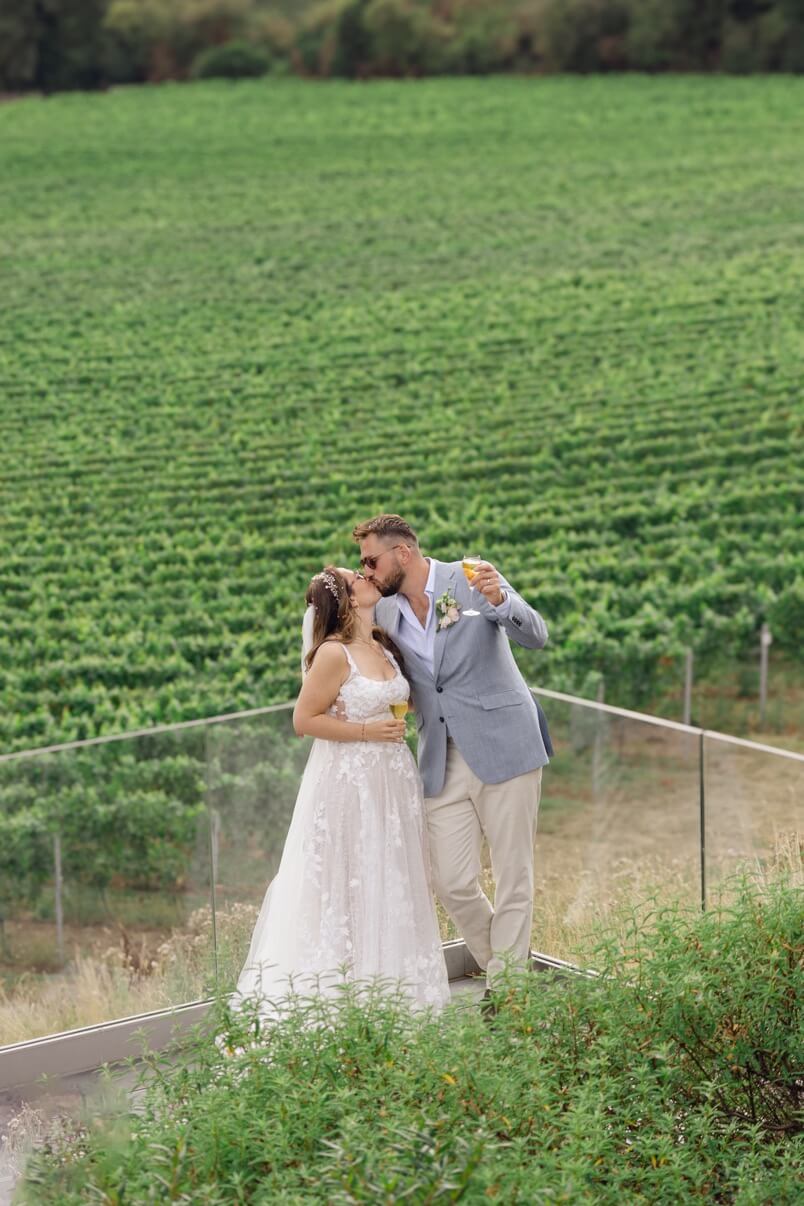 The bride and groom with drinks in front of the vineyard